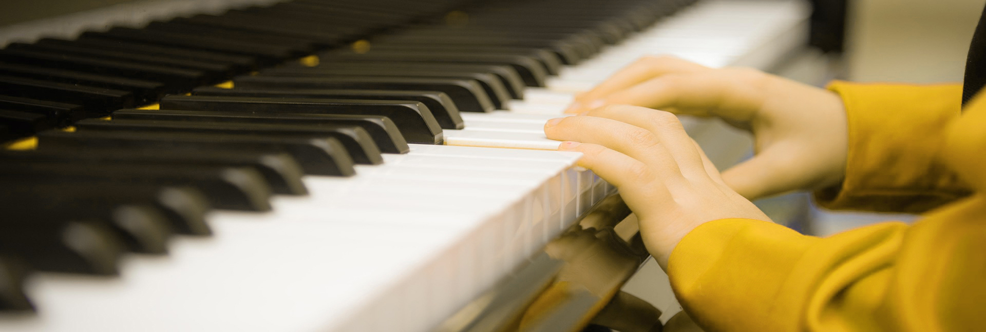 Hände einer Person mit gelbem Pullover am Klavier